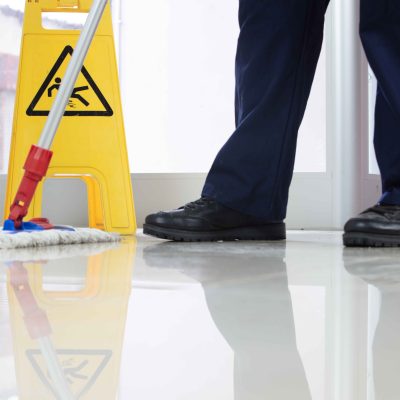 A low angle closeup of a person cleaning the floor with a mop near a yellow caution wet floor sign